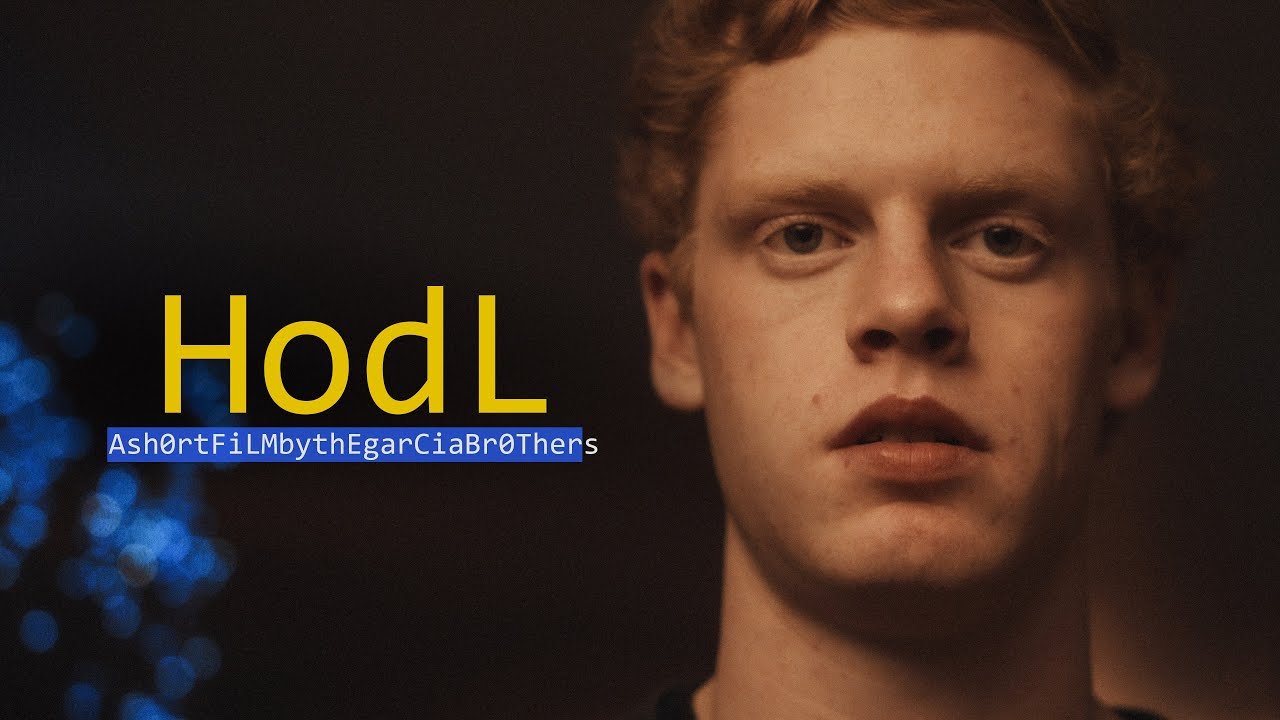 Dark, moody title card for HodL. A young man with curly auburn hair looks into the camera, lit in warm orange against blue out-of-focus lights. The title HodL is in large yellow letters on the left, with a short-film credit line to the Garcia Brothers below.